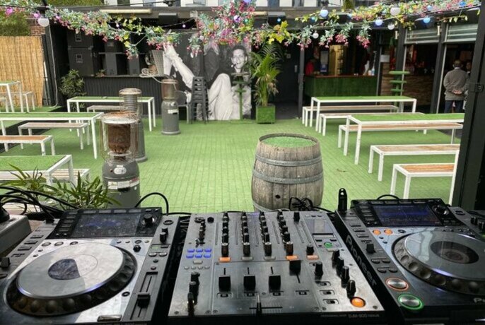 A grassy rooftop bar with a mural, flowers, and a DJ deck
