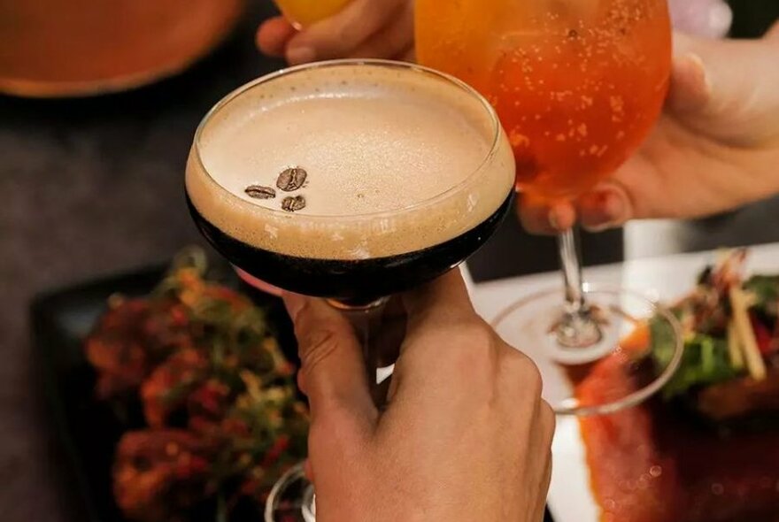 A hand holding an espresso martini over a table