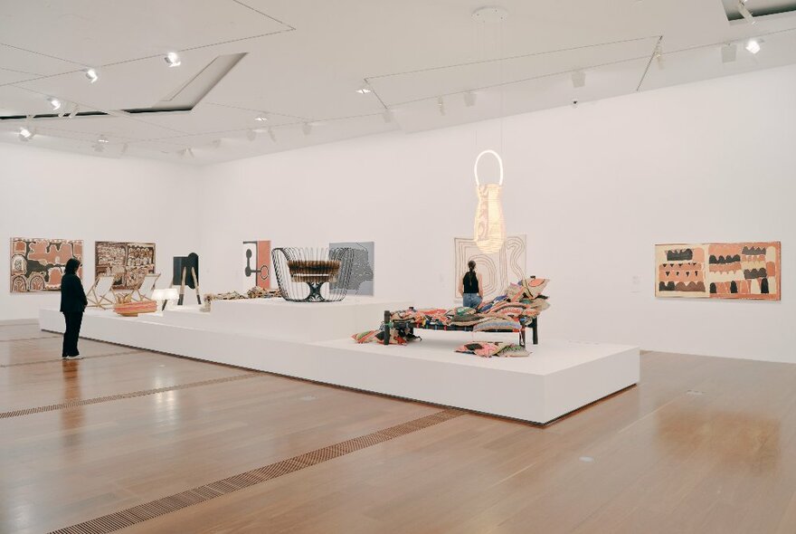A large gallery space with a white platform in the middle of the floor and various types of art displayed around the room. 