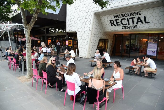 Exterior of Melbourne Recital Centre with patrons seated at tables and pink chairs.