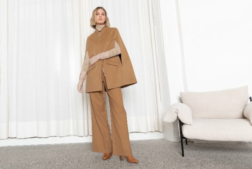 Model wearing a light brown trouser suit with cape detail.