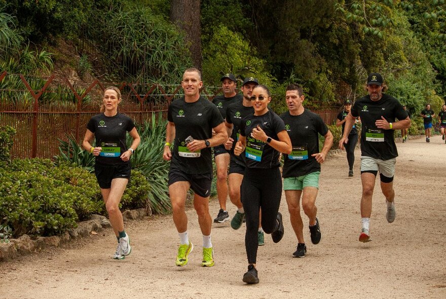 A team of runners wearing matching jogging outfits running along a sandy track beside foliage.
