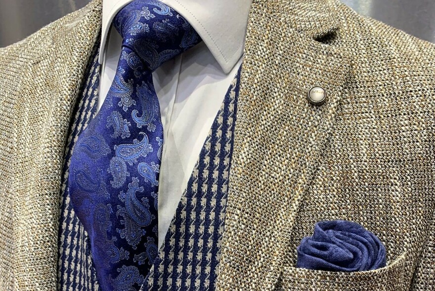 Grey jacket, black and white patterned waistcoat and a patterned blue silk tie.