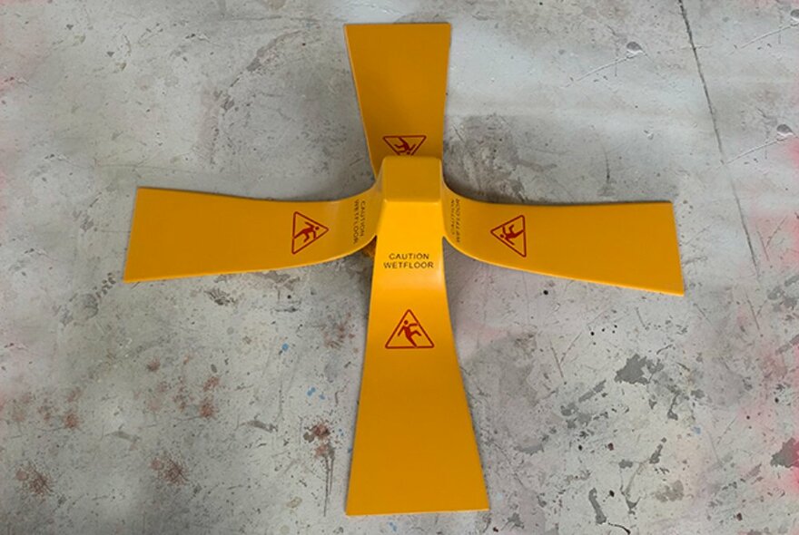 An orange safety barrier shaped like a cross, placed on the ground, to warn of a tripping hazard.