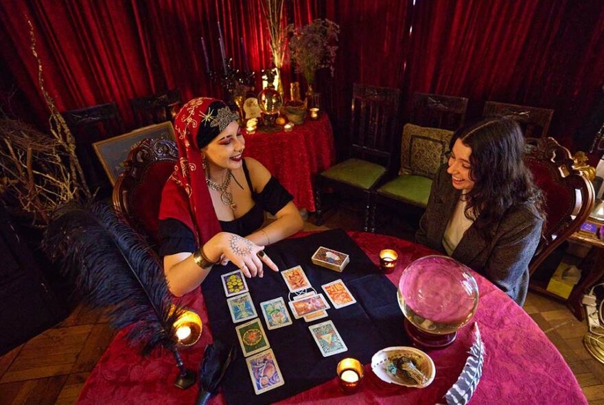 A tarot card reader reading a woman's cards in a cosy carpeted room.