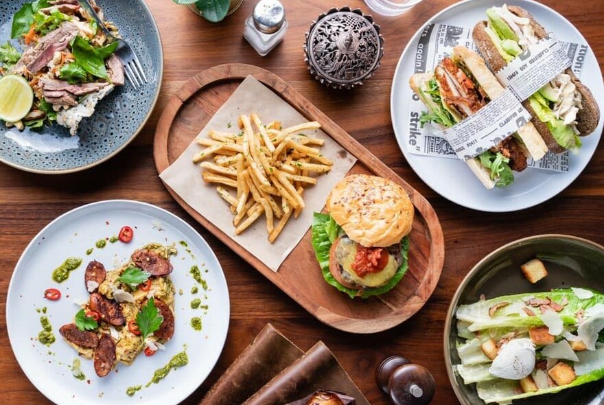 Various plates of food: salads, sandwiches and a burger and fries.