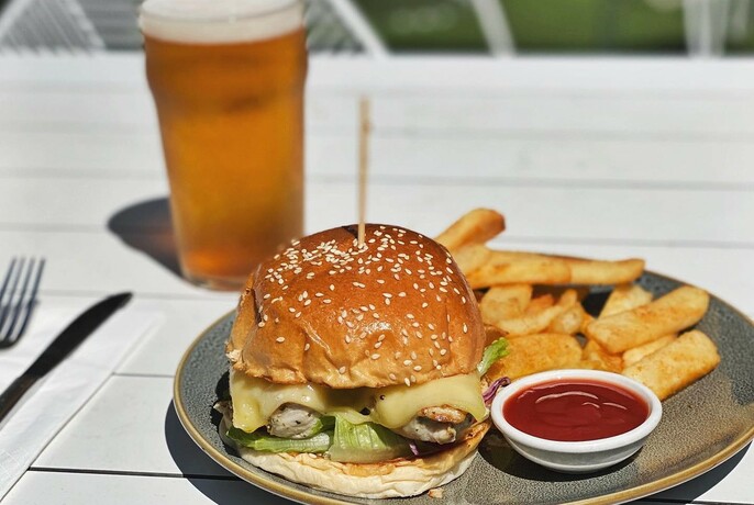 Outdoor table with glass of beer, hamburger and chips.