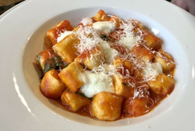 A white bowl of gnocchi with parmesan on top. 