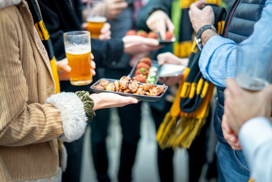 Person standing with a beer and small plate of tapas-style food.