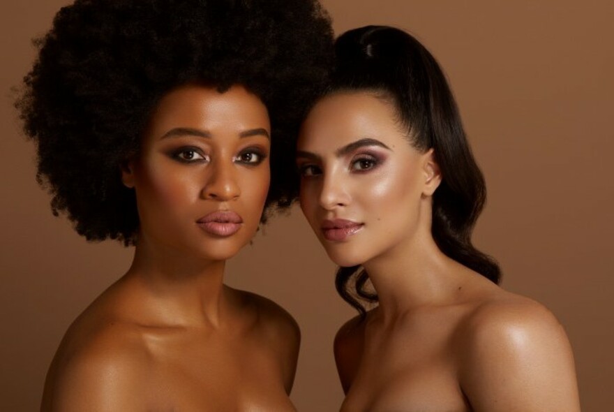 Two women with glowing skin looking straight ahead. 