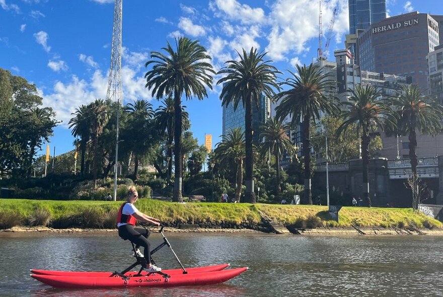 One single person red water bike on Yarra, cityscape at rear.