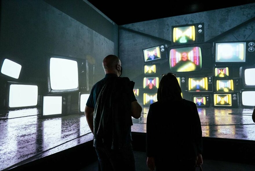 Museum visitors watching videos on multiple screens.