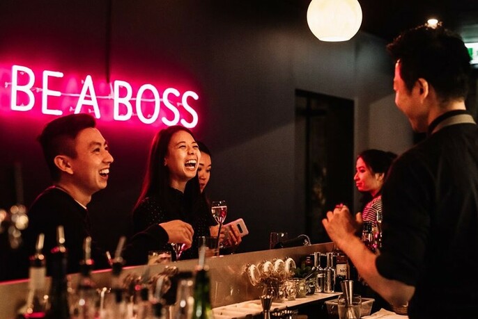 Men and women at the bar of Pincho Boss with a pink neon sign in the background. 
