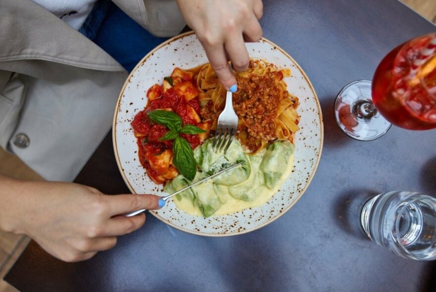 Someone eating from a plate with three different pastas. 