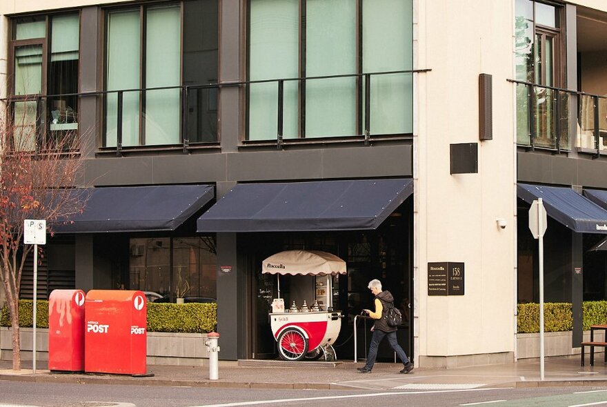 The exterior of a building with two large post boxes and an ice cream cart out the front. 