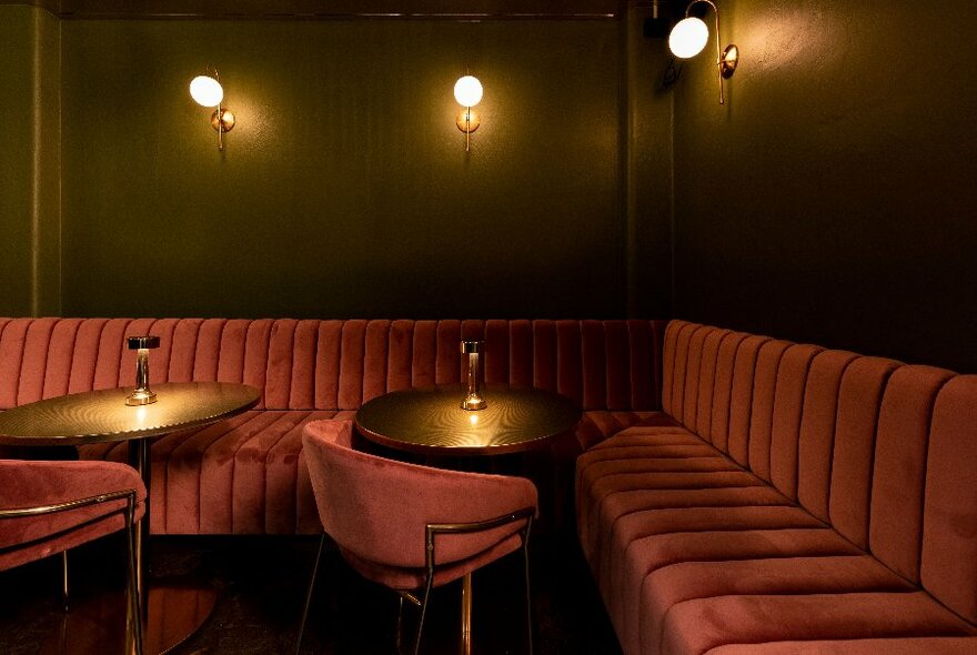A corner nook in a bar with red velvet bench seating.