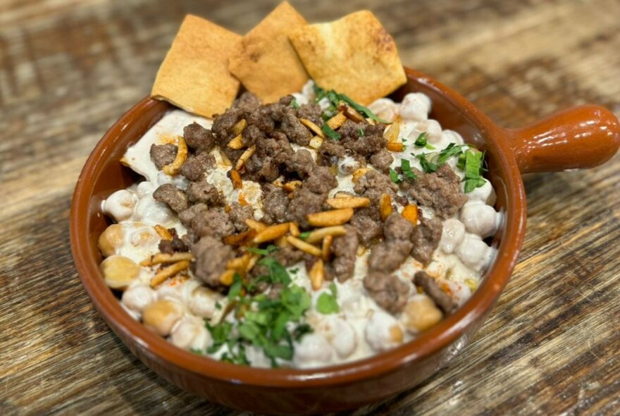 A small terracotta dish with chickpeas, meat, rice and a parsley garnish.