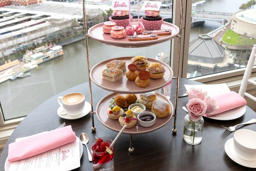 Pink-themed tiered tray of afternoon cakes on a table overlooking the Yarra.
