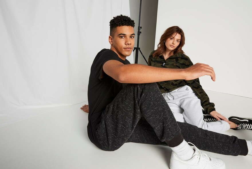 Male and female models seated in white photo shoot, wearing casual streetwear.
