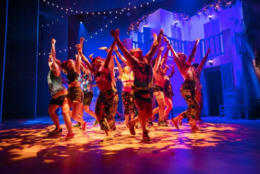 A group of actors on a theatre stage dancing around in a circle with their hands up in the air.