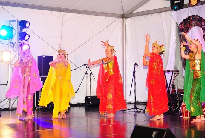 Colourfully dressed dancers performing on a stage in a tent.
