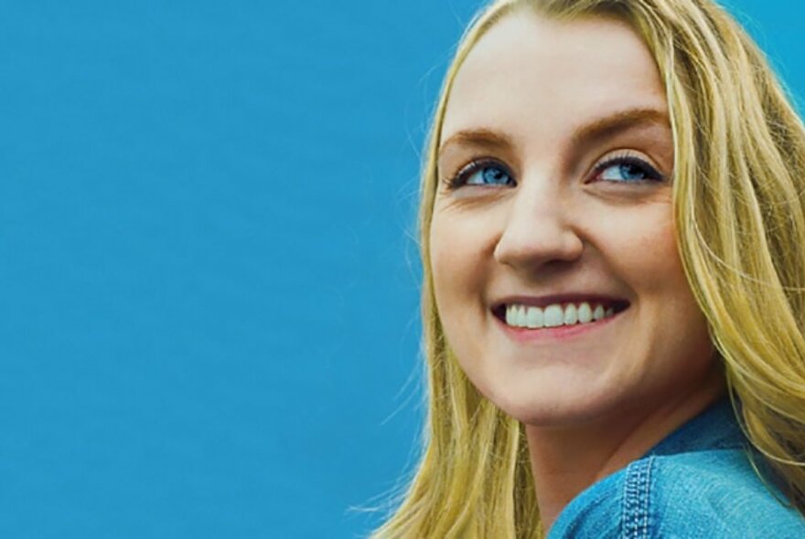 A smiling young woman with blond hair and blue eyes posed against a blue background.