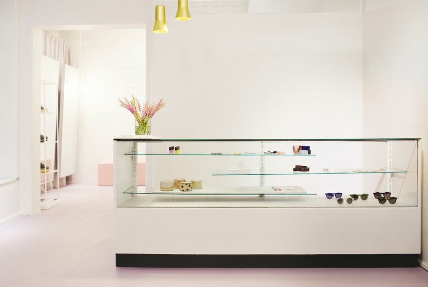 A modern, minimalist white shop interior with a display counter and two gold pendant lights. 