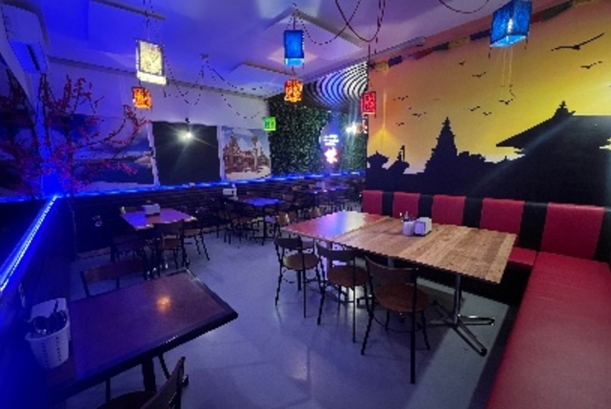 An empty cafe with several tables, a mural and dim coloured lights.