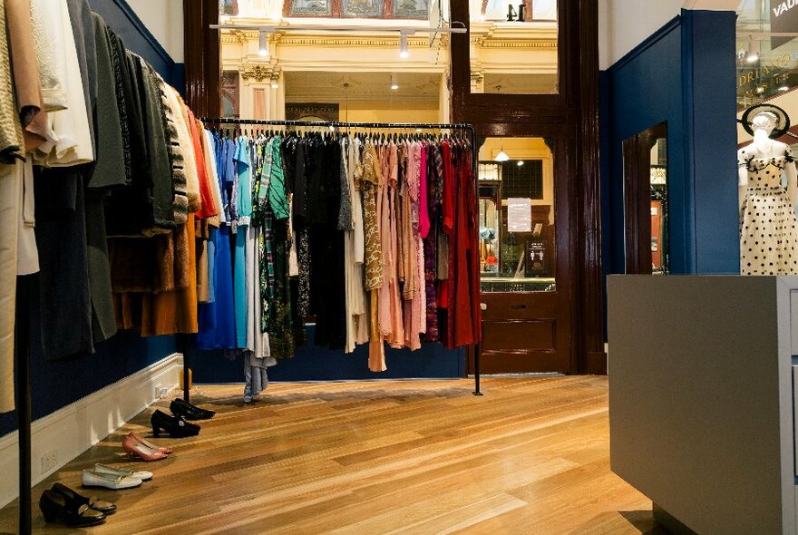 Interior of shop with racks of pre-loved designer clothes, and shoes resting on a wooden floor.