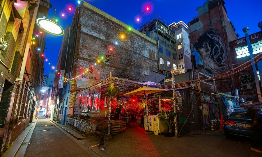 Night time wide shot of laneway brick bar with fairy lights and neon lights.
