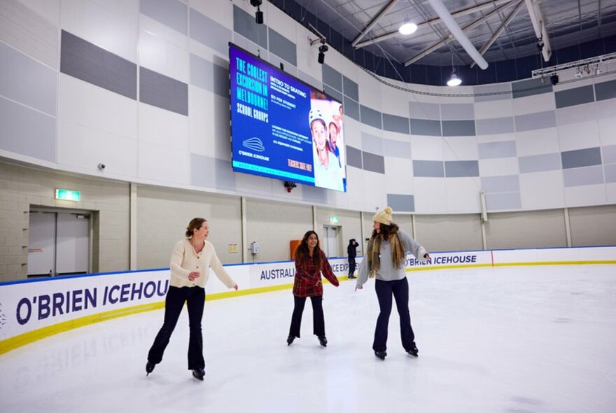 Three women skating on ice rink laughing with each other.