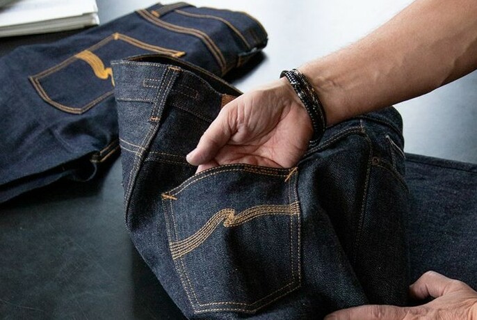 Nudie jeans on a table, with a hand showing off the Nudie pocket logo.
