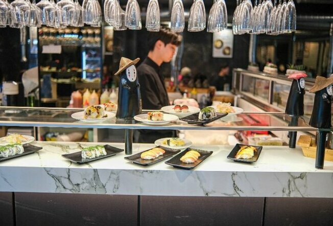 White marble bar with different sushi plates on top with chef behind the bar.