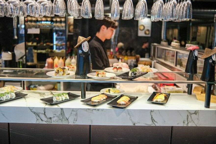 White marble bar with different sushi plates on top with chef behind the bar.