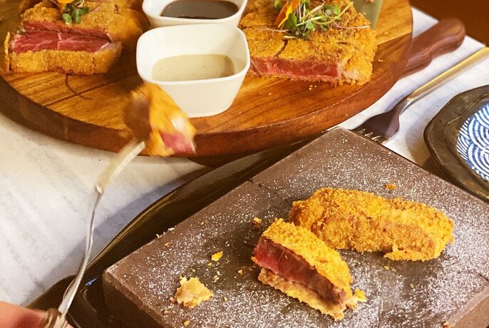 Someone taking a slice of crumbed beef off a platter.