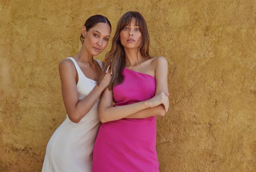 Two models wearing white and pink summer frocks against an earthy background.