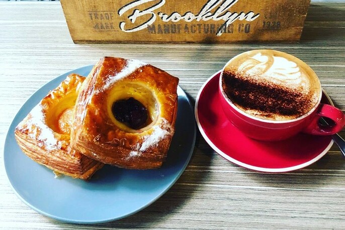 Table top with two Danish pastries on a blue saucer, red cup and saucer with coffee, and Brooklyn-branded coffee box.