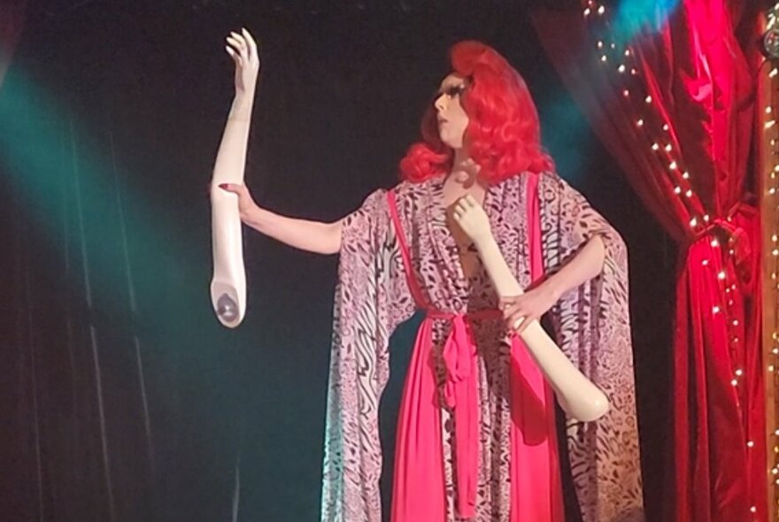A performer in costume on stage, holding the plastic arms of a mannequin in their hands.