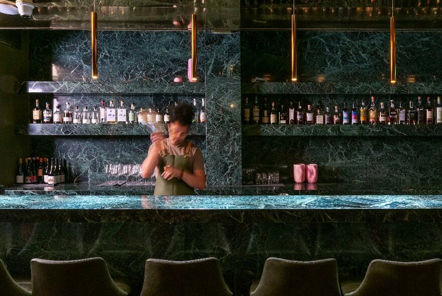A bartender shaking a cocktail behind a green marble bar. 