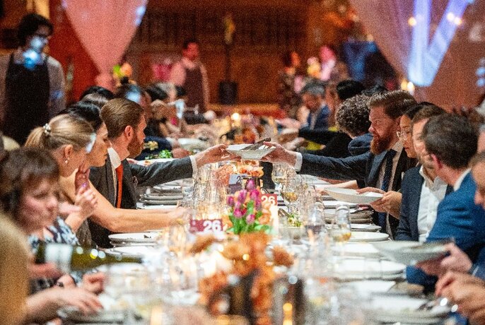People sitting down to a formal dinner at a very long table.