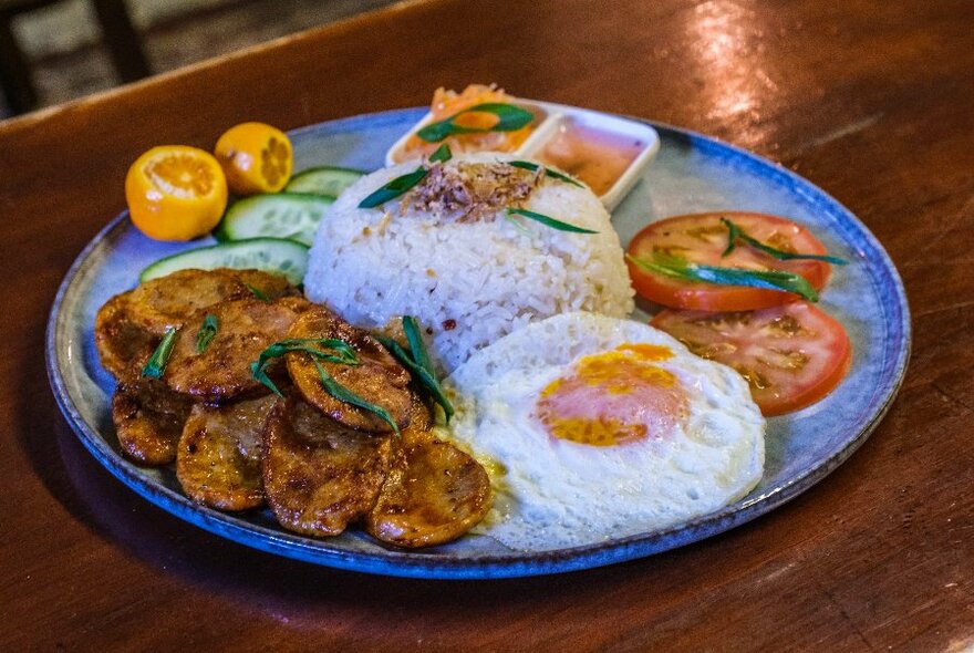 A plate of Filipino food with sausage, egg, rice, tomator and garnishes. 