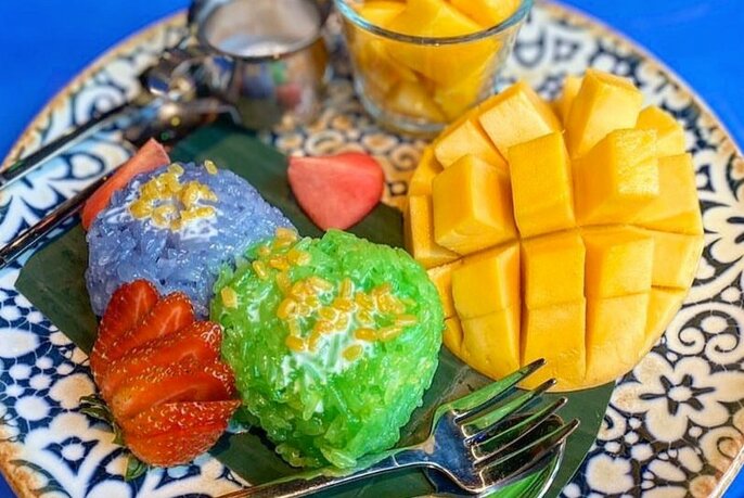 A plate with a colourful Thai dessert and fresh mango and strawberries. 