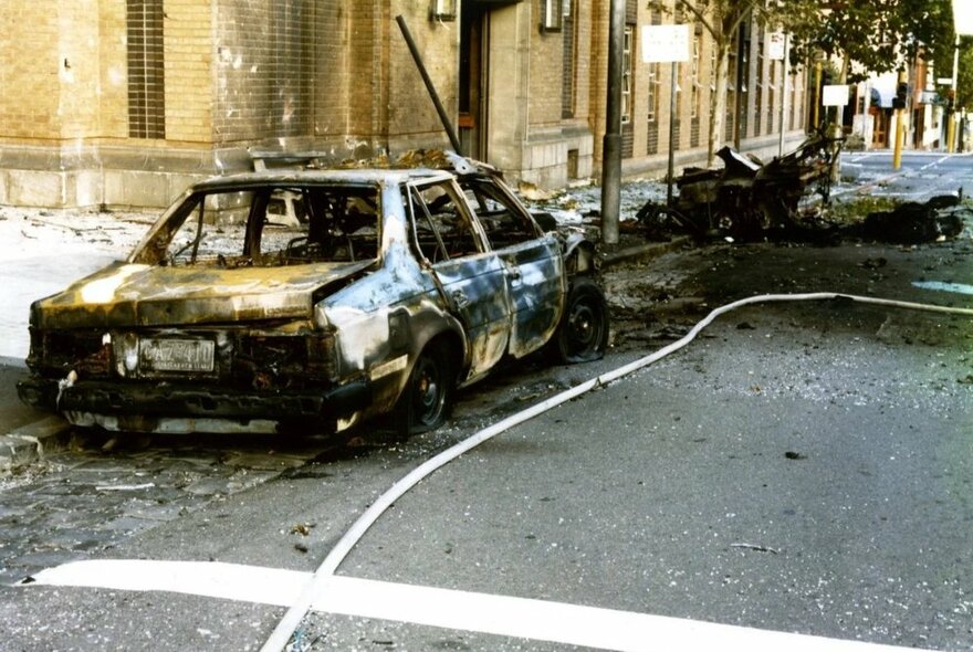 A burnt out shell of a car parked outside a building on a city street.