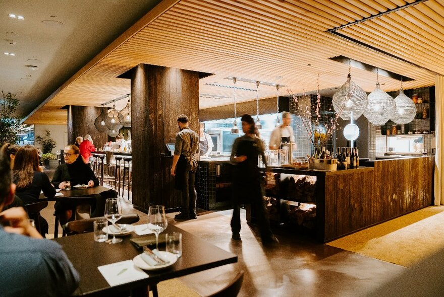 Modern wood-toned interior of a restaurant with staff in the background. 
