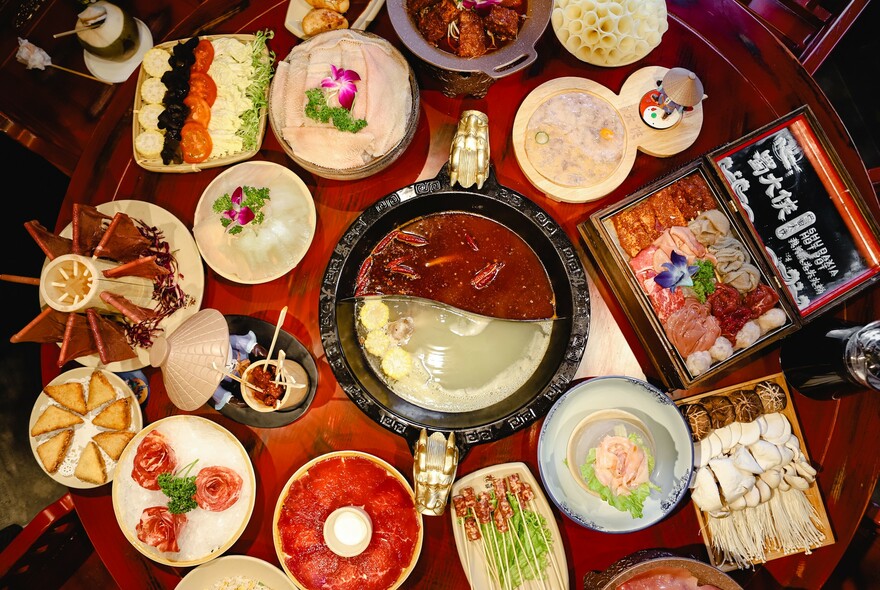 Chinese hot pot in yin and yang shape with small plates of ingredients around it.