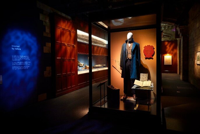 Installation view of an exhibition, with a clothed mannequin and books on display in a glass cabinet, with other items on display on the walls, and exhibition signage visible throughout.