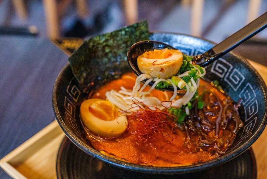 A spoon lifting an egg out of a bowl of ramen.