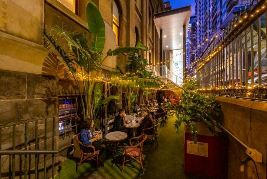 People sitting in the courtyard at a bar beneath fairy lights