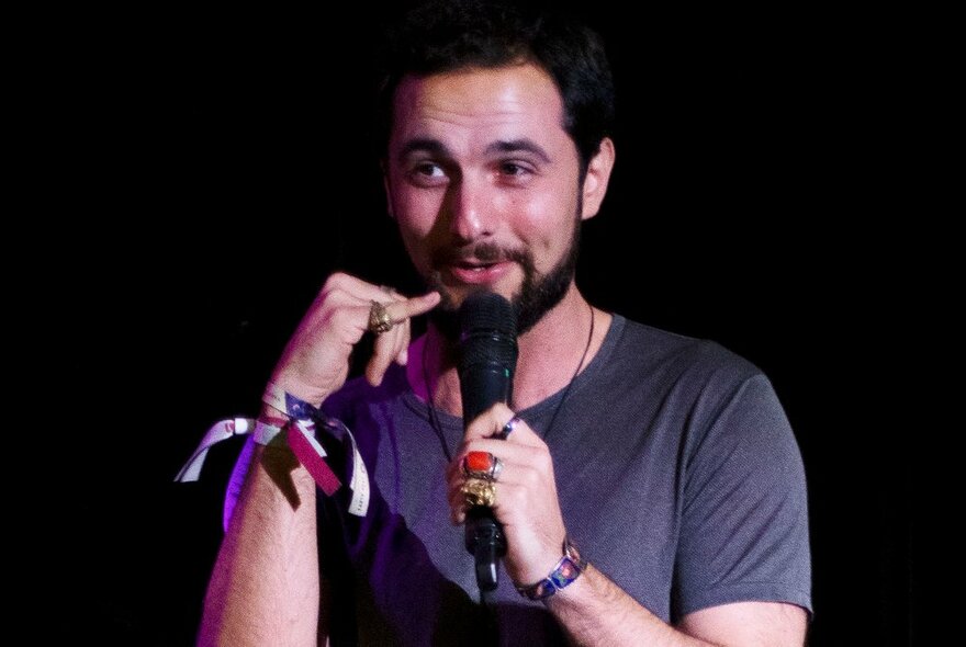 Man performing stand up comedy on a stage, holding a microphone.