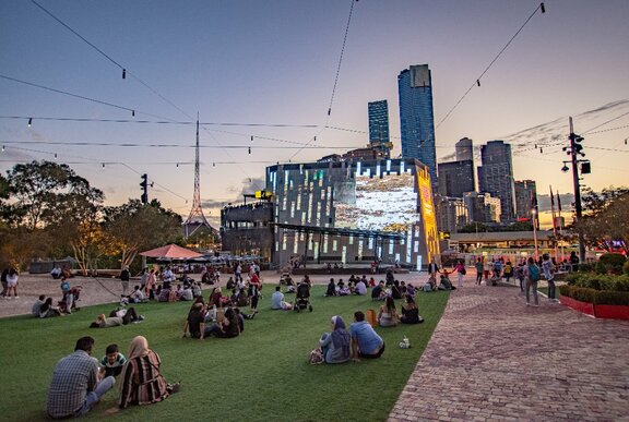 People sitting on the ground watching the Fed Square big screen in the city.